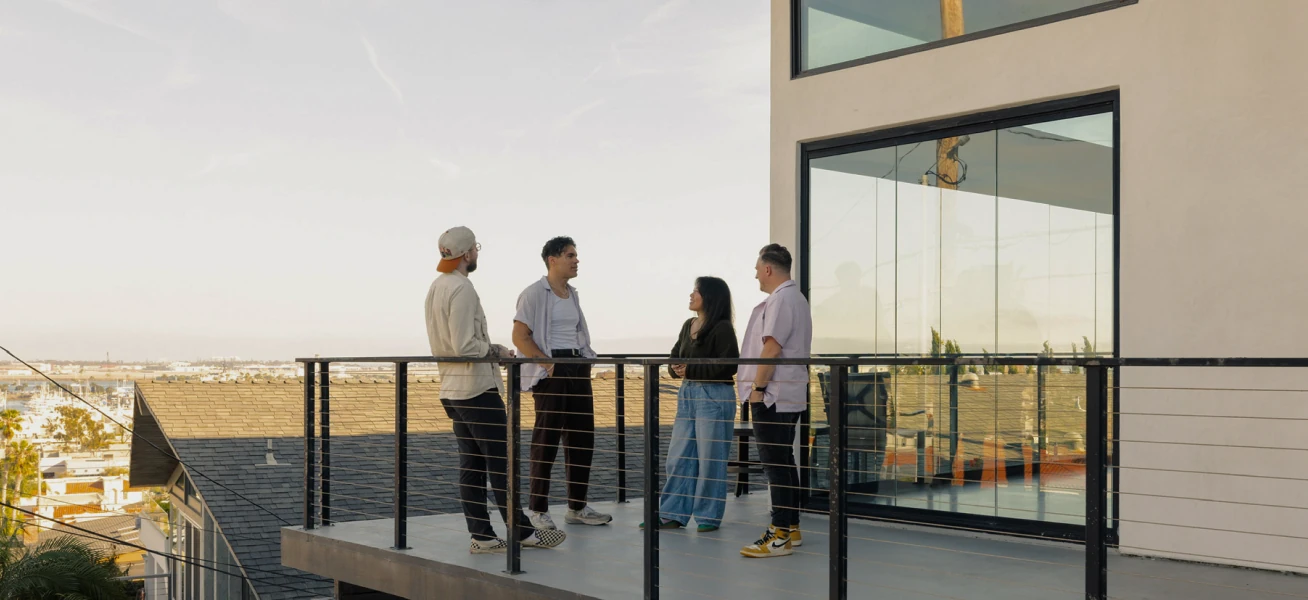Four Ballpark teammates talking on a sunlit balcony overlooking the city